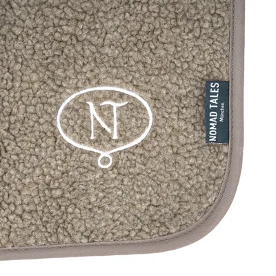 Tapis en tissu bouclé beige avec broderie NT dans une bulle et étiquette visible : NOMAD TALES München.
