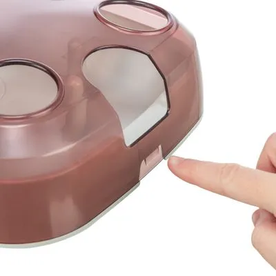 Vinger drukt op een plastic schuifmechanisme van een bruin doorzichtig apparaat met ronde openingen aan de bovenkant.