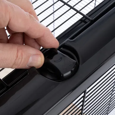 Close-up of a black locking mechanism on a wire cage being opened by a hand.