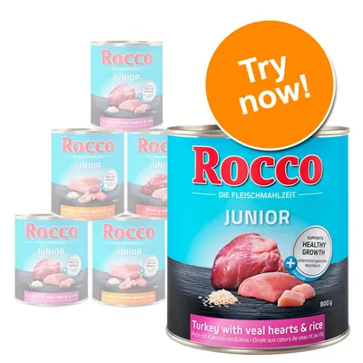 Rocco Junior wet dog food cans, visible flavours: turkey with veal hearts & rice, poultry chicken hearts & rice. Large can shows 'Supports healthy growth', 800g. Orange badge reads 'Try now!'.