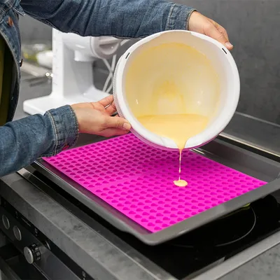 O persoană toarnă aluat dintr-un bol pe o tavă de copt din silicon roz cu forme de inimă, așezată pe o tavă de copt.