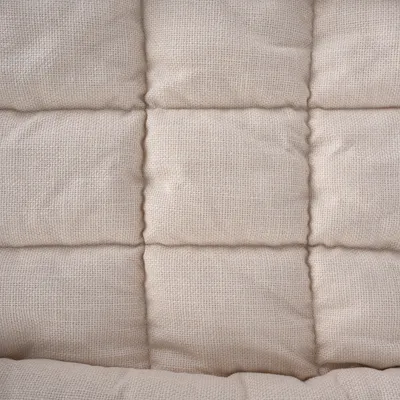 Primer plano de una superficie de tela beige acolchada con pespunteado cuadrado.
