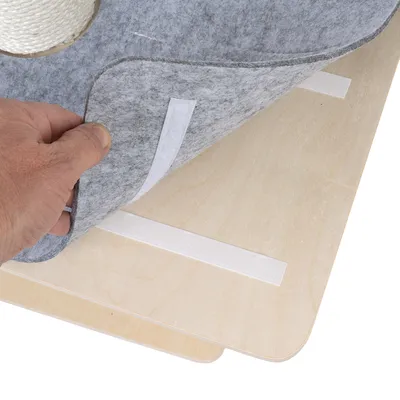Hand lifts grey felt mat with hook-and-loop fastener from a wooden board. Roll of white rope visible in the background.
