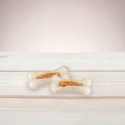 Due ossi per cani con ripieno visibile al centro, su superficie in legno chiaro. Nessun marchio o testo visibile.