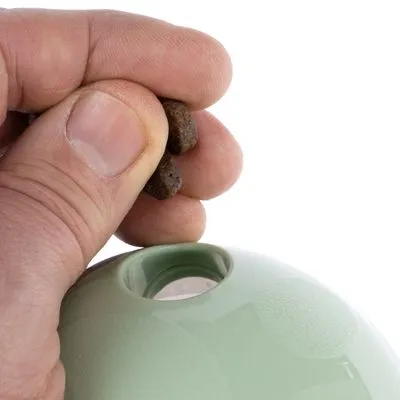 Hand vult groene kunststof bal met brokjes via opening aan de bovenkant.