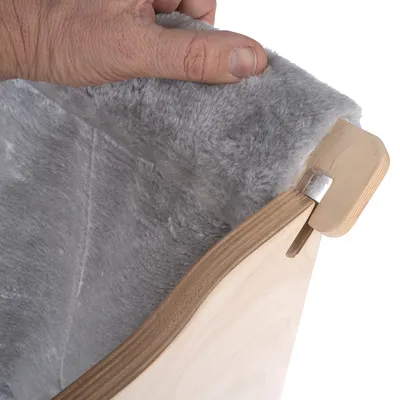 Nahaufnahme einer Hand, die eine graue, weiche Stoffpolsterung auf einem Holzrahmen anhebt. Zeigt Materialqualität und Verarbeitung.