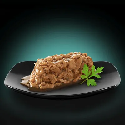 Close-up of a piece of meat in sauce on a black plate, garnished with a green parsley leaf.