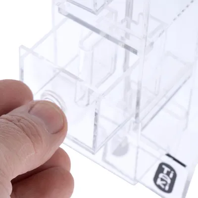 Main ouvrant un tiroir d’un distributeur transparent en plastique, logo TiKi visible sur le coin inférieur droit.