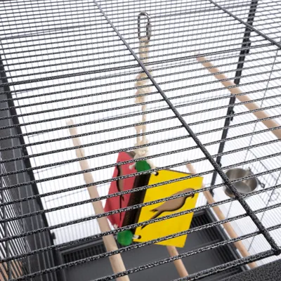 Vogelkäfig mit Metallgitter, Holzstangen und hängendem Spielzeug in Rot und Gelb.