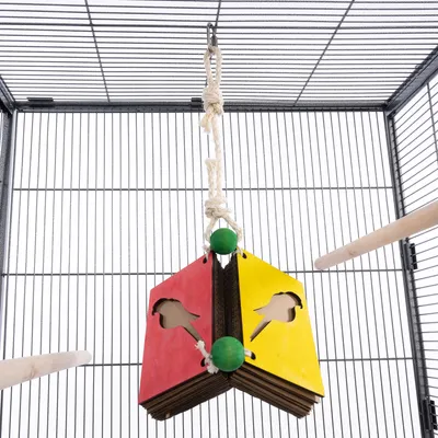 Hängendes Vogelspielzeug aus Pappe mit roten und gelben Holzplatten, grünen Kugeln und Seilbefestigung in einem Käfig.