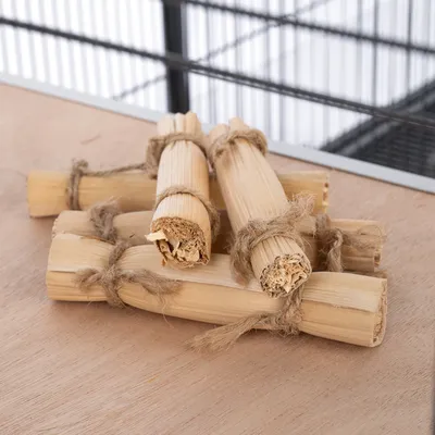 Bâtonnets de bois naturel attachés avec de la ficelle, posés sur une surface en bois devant une cage métallique.