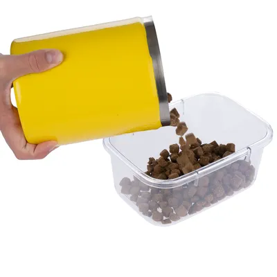 Hand giet bruine brokjes droogvoer uit een gele container in een doorzichtige plastic box.