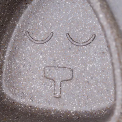 Nahaufnahme einer grauen Oberfläche mit eingraviertem Symbol: zwei geschlossene Augen und eine Nase in Form eines T. Symbol möglicherweise dekorativ oder funktional.