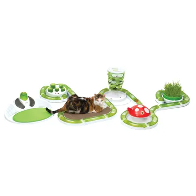 Interaktives Katzenspielzeug-Set mit verschiedenen Modulen: Kratzmatte, Futterturm, Grasbehälter, Spielbahn und rotem Pilz-Spielzeug. Katze liegt auf der Kratzmatte.