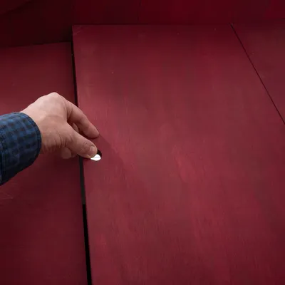 Hand öffnet eine rote Holzplatte mit eingelassenem Griff. Demonstration der Bedienung eines Möbelstücks oder einer Abdeckung.