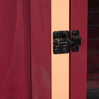 Detailansicht eines schwarzen Metallverschlusses an einer rot-braunen Holztür mit hellem Rahmen.