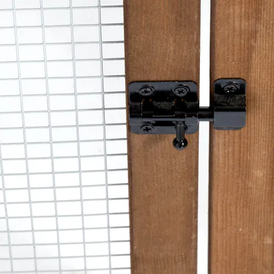 Gros plan sur un loquet en métal noir fixé sur une porte en bois avec grillage métallique à mailles carrées visibles.