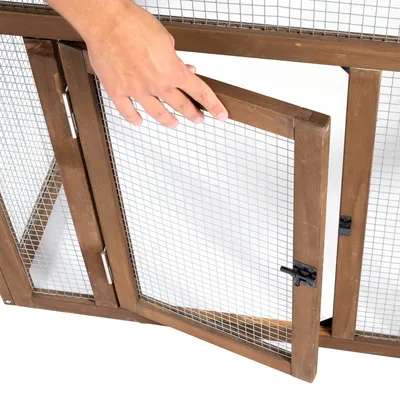 Porte en bois et grillage métallique d’une cage ou enclos, ouverte à la main, avec loquet noir visible.