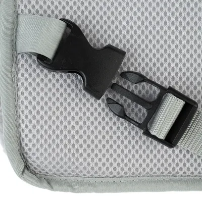 Gros plan sur une boucle en plastique noir avec sangle grise, fixée à un tissu maillé gris clair. Matériaux visibles : plastique et tissu.