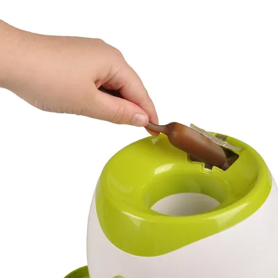 Main insérant une friandise marron dans un distributeur vert et blanc en plastique, ouverture visible sur le dessus de l’appareil.