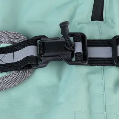 Gros plan sur une boucle en plastique noir avec sangle réfléchissante grise, fixée sur un tissu vert clair et une bordure en nylon gris.