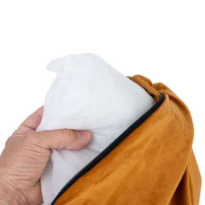 Hand zeigt das Einlegen eines weissen Kissens in einen senfgelben Bezug mit Reissverschluss.