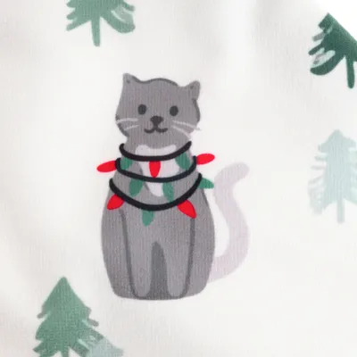 Illustration av en grå katt med ljusslinga och gröna blad, omgiven av stiliserade granar.