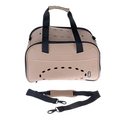 Sac de transport beige TIAKI avec poignées noires, trous d’aération sur le dessus et le côté, bandoulière amovible posée devant le sac. Marque TIAKI visible.