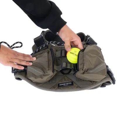 Nomad Tales Hundegeschirr mit Taschen, eine Hand legt einen gelben Nomad Tales Ball in die Reissverschlusstasche.