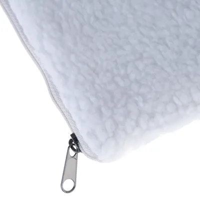 Gros plan sur un coin de coussin blanc en tissu polaire avec fermeture éclair métallique visible.