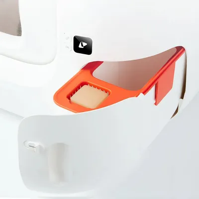 Compartiment orange avec filtre rectangulaire visible dans une litière pour chat blanche, bouton noir avec symbole flèche et levier blanc marqué OPEN.