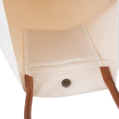 Vista interior de un bolso beige de tela con cierre magnético y asas marrones.