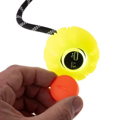Gul bold med USB-port og tænd/sluk-knap, orange indsats holdes i hånden. Sort snor med reflekterende striber synlig.
