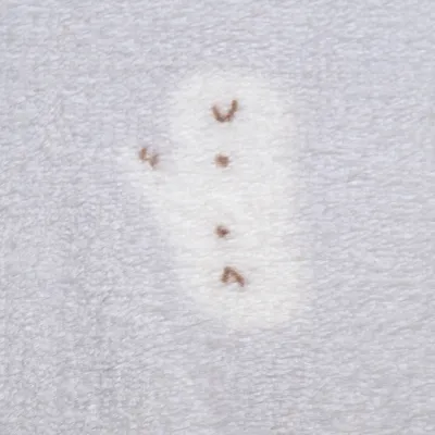 Détail de tissu peluche gris clair avec motif animal stylisé en blanc et marron, matière douce visible.