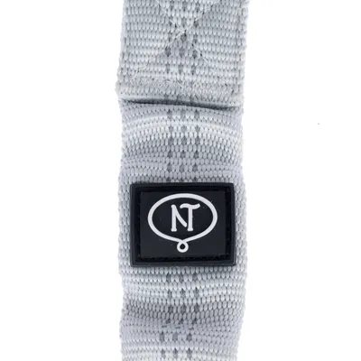 Sangle en tissu gris avec écusson noir affichant le texte NT dans un ovale blanc. Aucun autre détail visible.