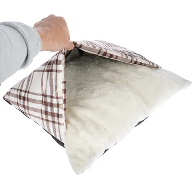 Kéz kinyit egy barna-fehér kockás huzatú párnát puha, fehér plüss töltettel.