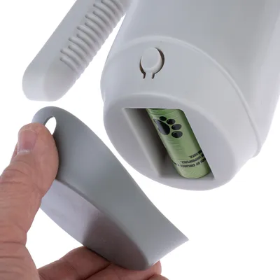 Dispensador blanco con asa y compartimento para rollo de bolsas verdes para excrementos de perro. Tapa gris extraíble a mano.