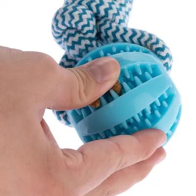 Mano introduce golosinas en una pelota de juego azul con protuberancias y una cuerda de tela anudada. Muestra el uso del juguete para rellenar con snacks.