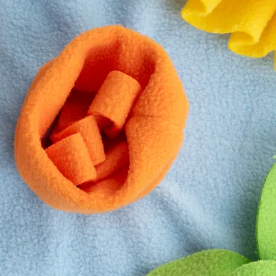 Orange fleece-legetøj i blomsterform på lyseblå baggrund, egnet til interaktiv leg eller aktivering.