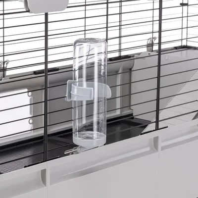 Transparente Trinkflasche mit weisser Halterung, befestigt an einem Metallgitter eines Käfigs.