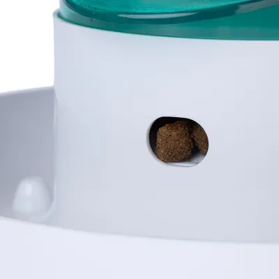 Nahaufnahme eines weissen Futterspenders mit grünem Deckel, der Trockenfutter durch eine kleine Öffnung ausgibt.
