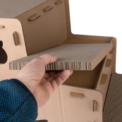 Hand zeigt herausnehmbare Pappelemente eines modularen Kratzmöbels aus Wellpappe mit Stecksystem.
