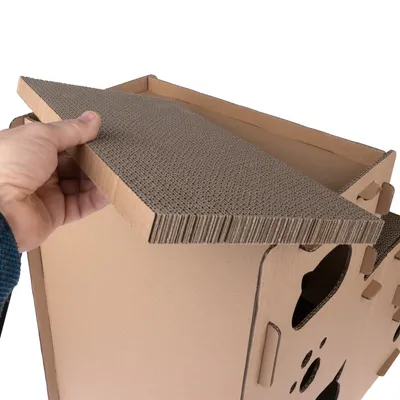Hand hebt ein Dach aus Wellpappe von einem Kartonhaus mit Ausschnitten. Zeigt abnehmbares Design und Materialstruktur.