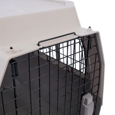 Szállítóbox fekete fémráccsal, bézs műanyag házzal és felső fogantyúval. Elöl látható zárómechanizmus.