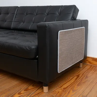 Kratzschutzmatte aus Sisal, befestigt an der Armlehne eines schwarzen Ledersofas. Matte schützt Möbel vor Kratzspuren.
