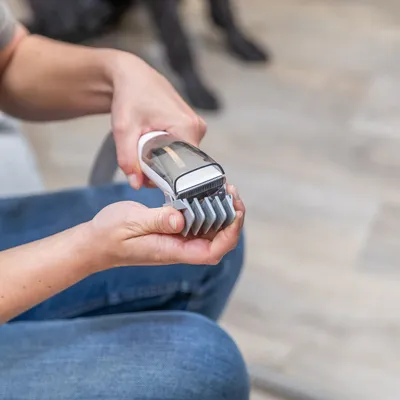 Mano sostiene una máquina eléctrica para cortar pelo de mascotas con accesorio gris, adecuada para recortes precisos.