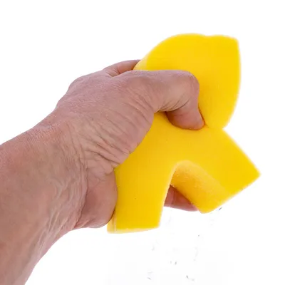 Gelber Reinigungsschwamm in Tierform, wird von einer Hand zusammengedrückt, Wasser tropft heraus.