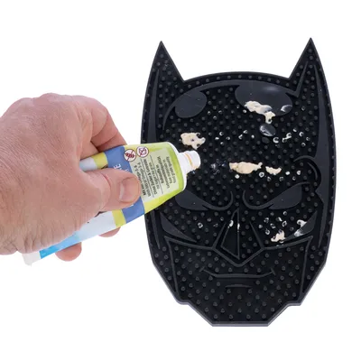 Hand applicerar pasta på svart silikonmatta med Batman-design. Mattan har strukturerad yta för jämn fördelning.