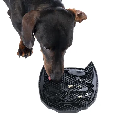 Hund slickar matrester från en svart slickmatta i kattform med strukturerade ytor.