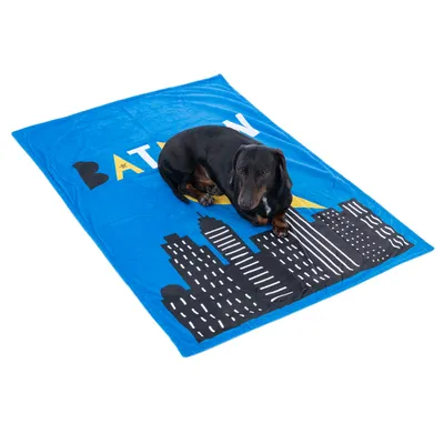 Dog lying on a blue blanket with Batman design and skyline motif.